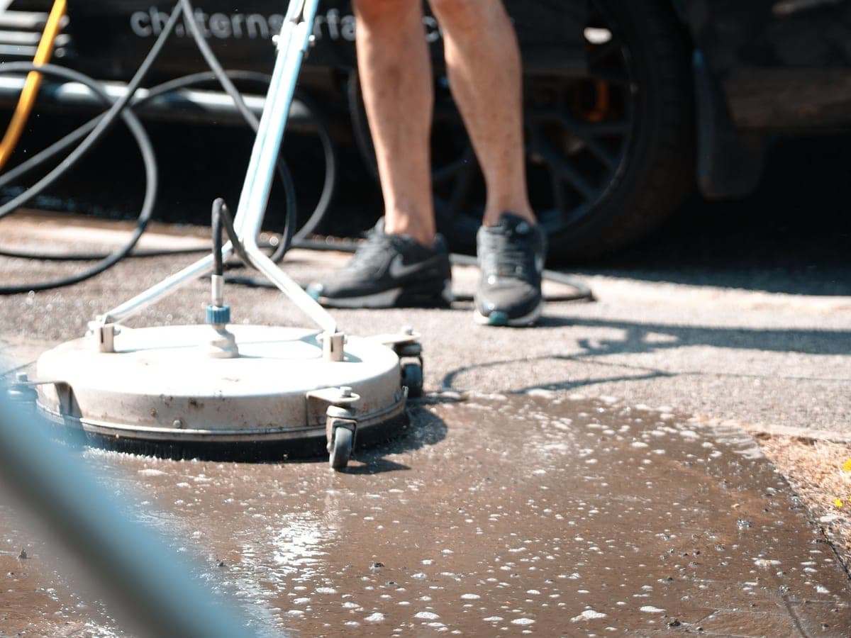 Rotary surface cleaner working across a wet driveway, foam lifting the dirt out of the surface