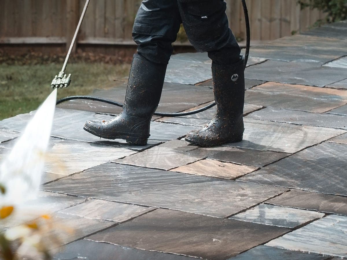 Natural stone patio being pressure washed, individual flags and the spray fan clearly visible